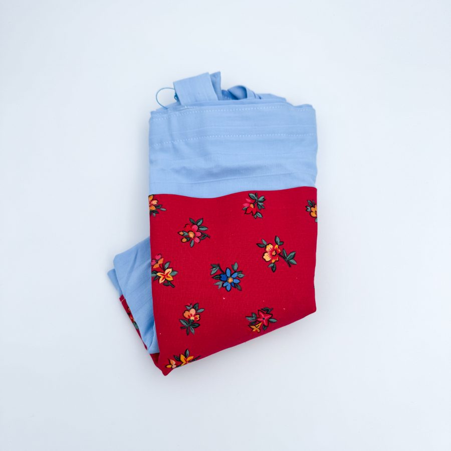 blåt materiale med en rød lomme med blomster. Hanken er blå.