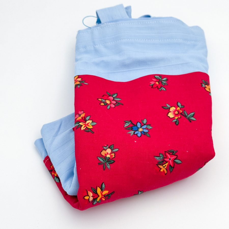 blåt materiale med en rød lomme med blomster. Hanken er blå.