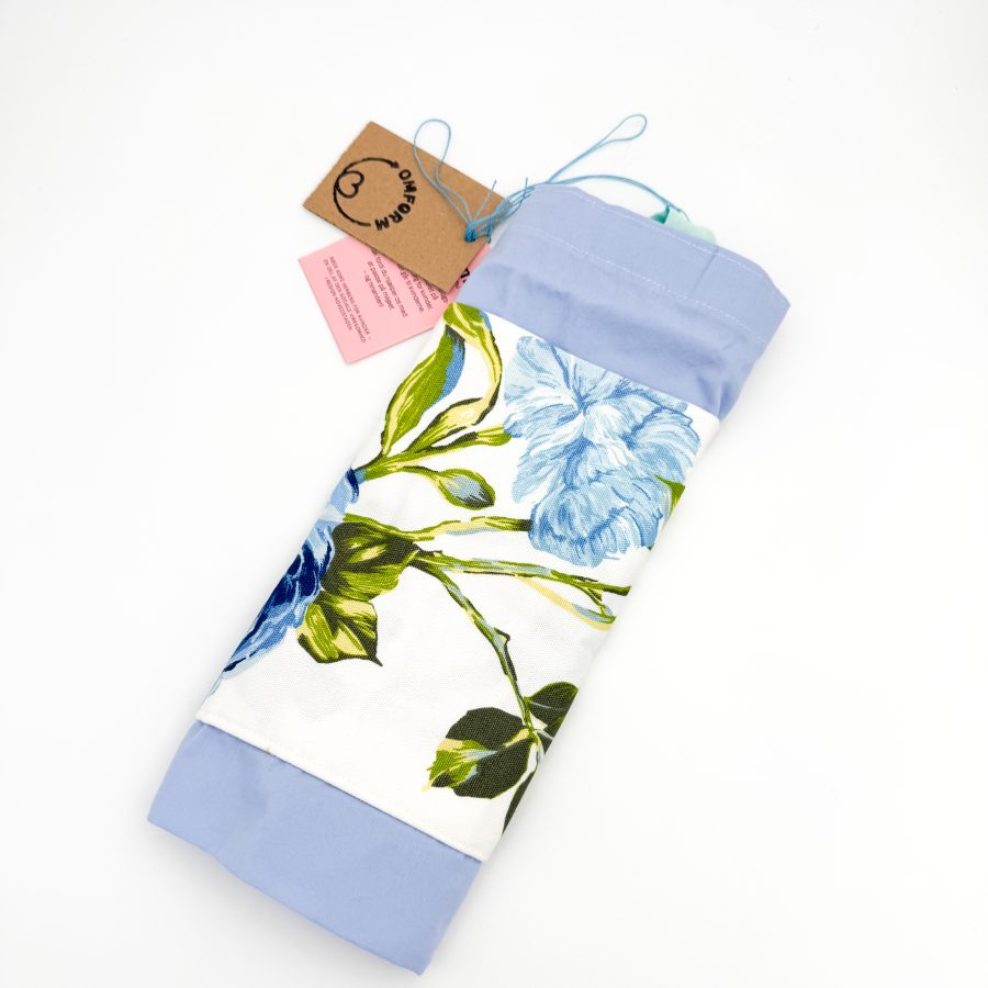 blåt materiale med en hvid lomme med blomster. Hanken er turkis.