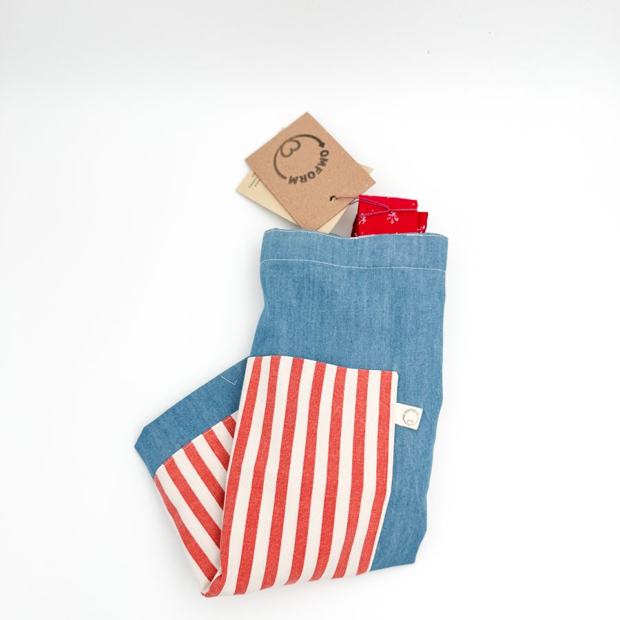 denim blåt materiale med rød og hvid stribet lomme. Hanken er rød med et hvidt mønster.