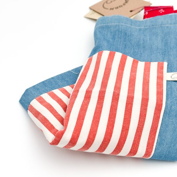 denim blåt materiale med rød og hvid stribet lomme. Hanken er rød med et hvidt mønster.