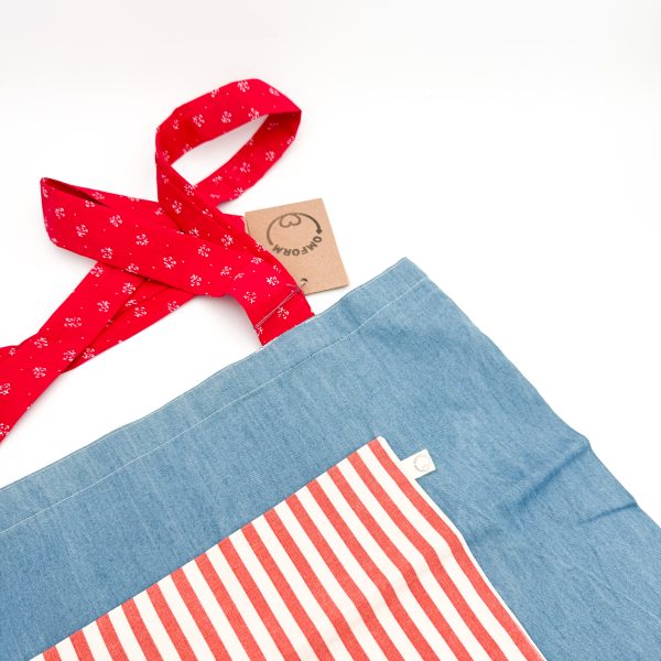 denim blåt materiale med rød og hvid stribet lomme. Hanken er rød med et hvidt mønster.
