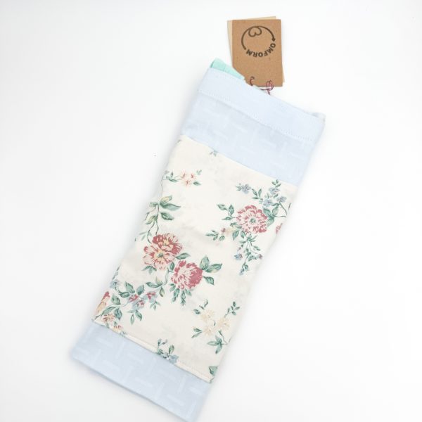 lyseblå materiale med motiv og en beige lomme med blomster. Hanken er turkis.
