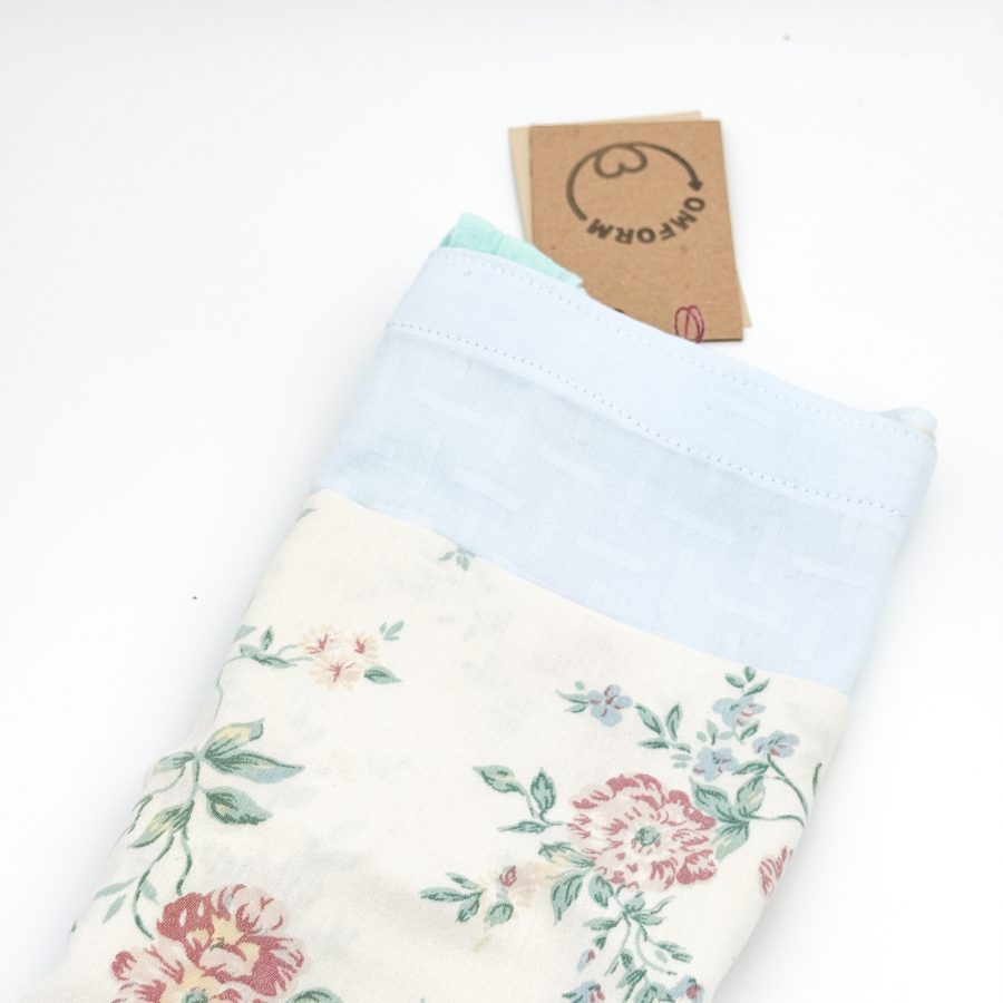 lyseblå materiale med motiv og en beige lomme med blomster. Hanken er turkis.