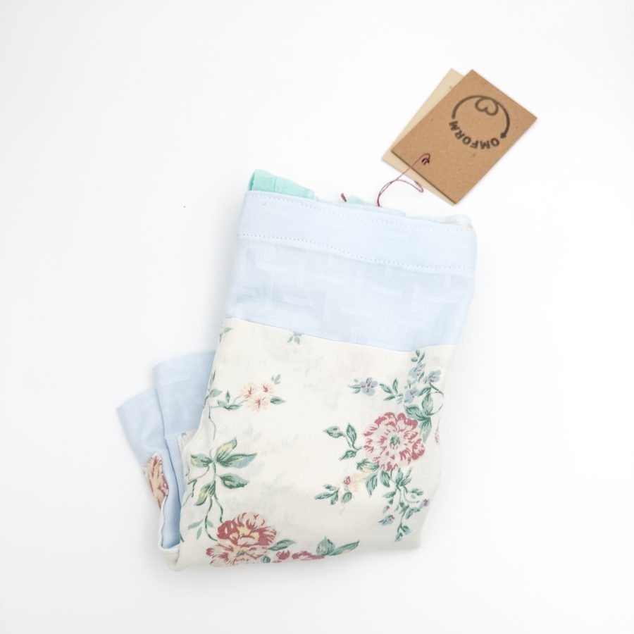 lyseblå materiale med motiv og en beige lomme med blomster. Hanken er turkis.