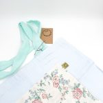 lyseblå materiale med motiv og en beige lomme med blomster. Hanken er turkis.