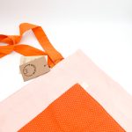 Dette net er af et fersken farvet materiale med lidt motiv på. Den har en orange lomme med hvide prikker og en orange hank.
