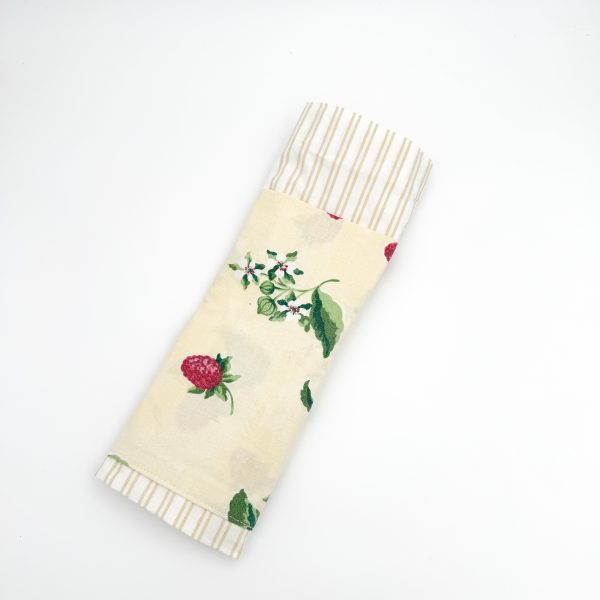 hvid stribet materiale med en gul lomme hvor på der er blomster og hindbær. Hanken er af samme materiale som lommen.