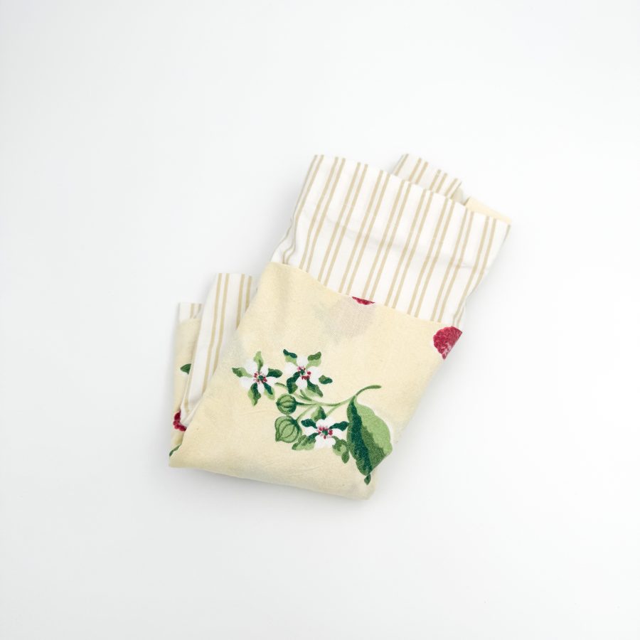 hvid stribet materiale med en gul lomme hvor på der er blomster og hindbær. Hanken er af samme materiale som lommen.