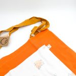 Dette net er af et orange materiale med hvid blomstret lomme og en mørkegul hank.